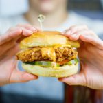 a picture focused on a fried chicken sandwich gripped by a person who holds it out to the camera.