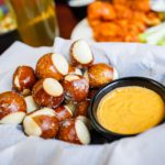 A paper-lined basket with round pretzel balls with a cup of honey mustard