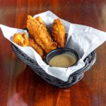 a paper-lined basket with chicken fingers and a cup of honey mustard.