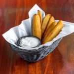 a basket holding fried pickle slivers and a cup of ranch