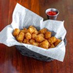a paper-lined basket filled with tater tots, to the side there is a cup of ketchup